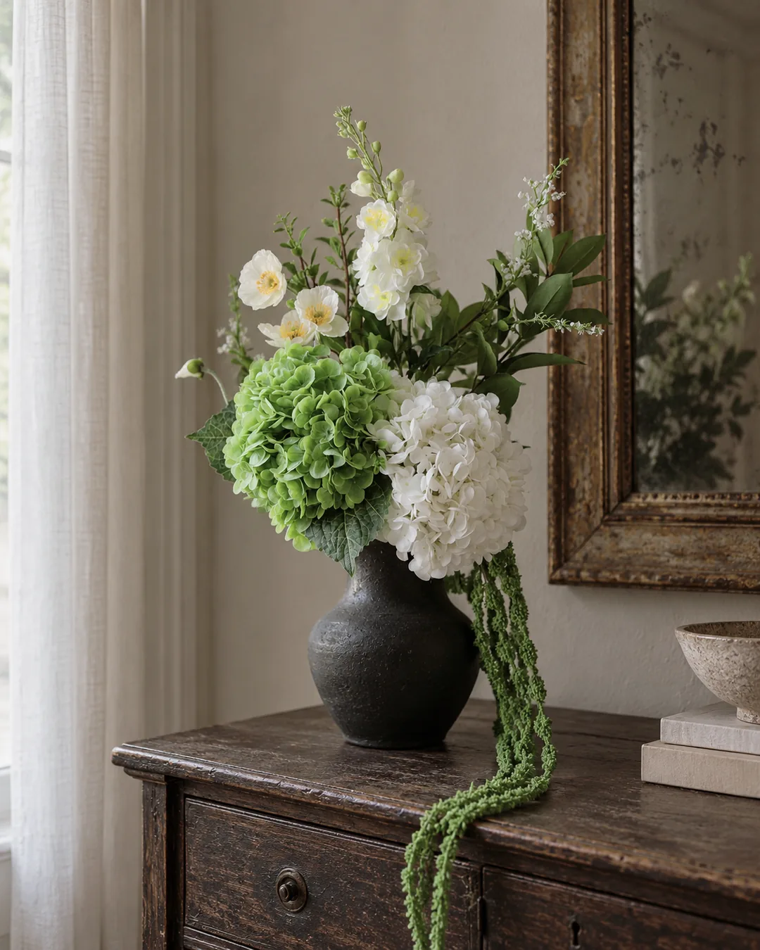 White and green flowers in a dark vase beside a sunlit window
